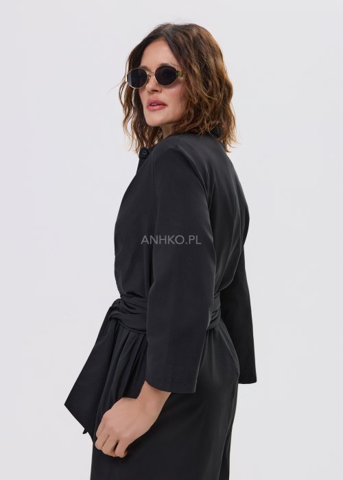 Czarny kombinezon damski z kopertową górą i paskiem w talii, z długim rękawem i szerokimi nogawkami, stylizowany z sandałami na obcasie.