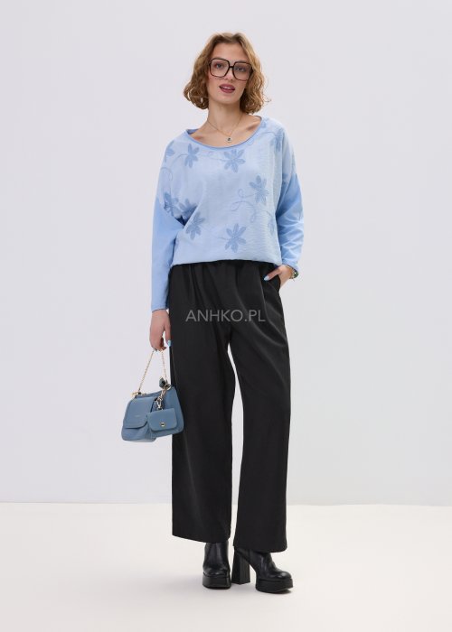 Niebieska bluzka damska oversize z haftowanym wzorem kwiatowym, z długim rękawem i szerokim dekoltem, stylizowana z czarnymi spodniami.