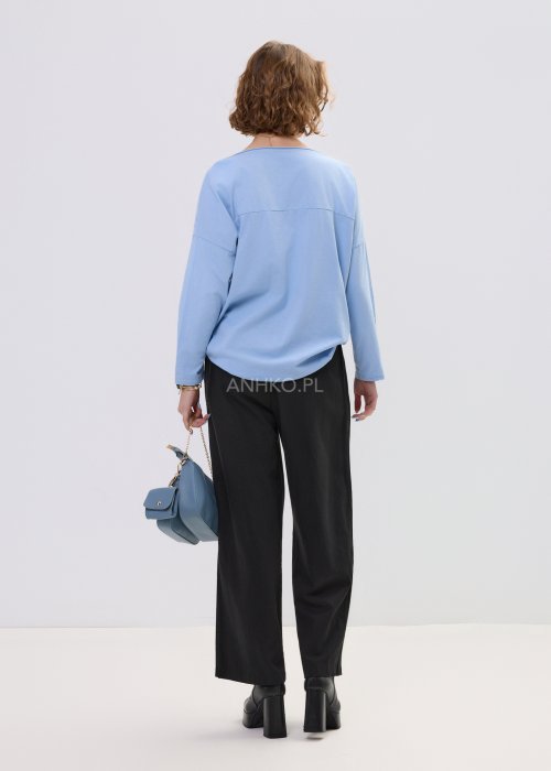 Niebieska bluzka damska oversize z haftowanym wzorem kwiatowym, z długim rękawem i szerokim dekoltem, stylizowana z czarnymi spodniami.