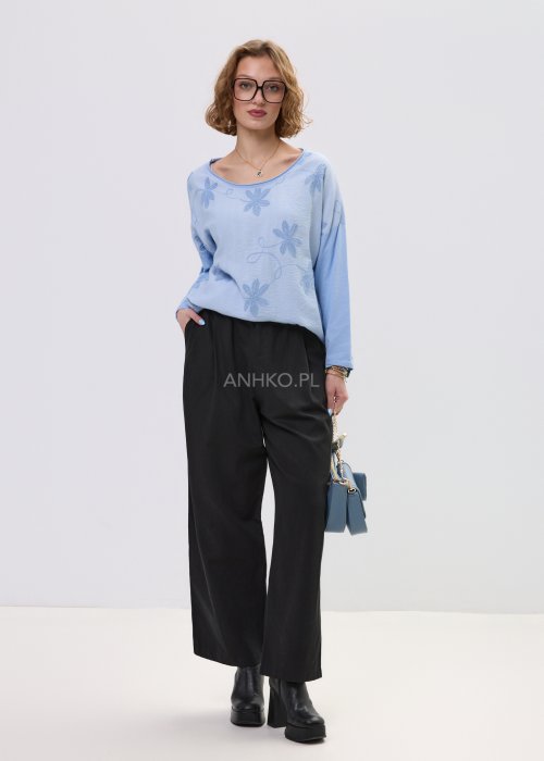 Niebieska bluzka damska oversize z haftowanym wzorem kwiatowym, z długim rękawem i szerokim dekoltem, stylizowana z czarnymi spodniami.
