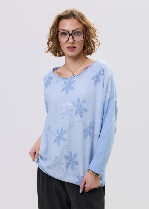 Niebieska bluzka damska oversize z haftowanym wzorem kwiatowym, z długim rękawem i szerokim dekoltem, stylizowana z czarnymi spodniami.