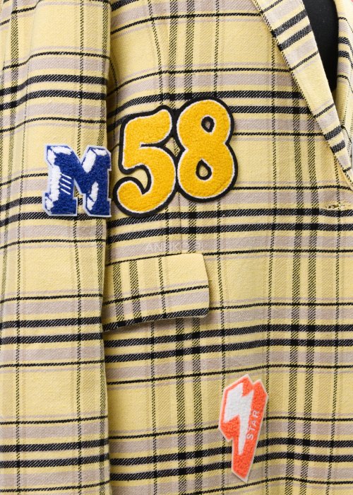 Marynarka damska w żółtą kratę z kolorowymi naszywkami literowymi, o luźnym kroju z klapami, stylizowany z czarnym topem i spodniami.