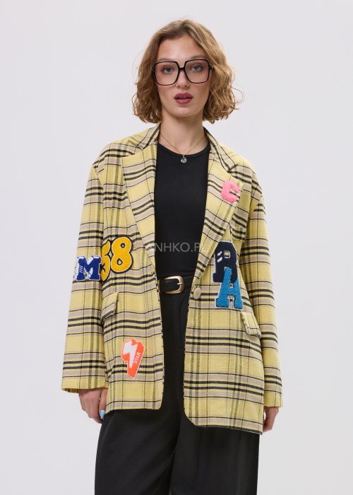 Marynarka damska w żółtą kratę z kolorowymi naszywkami literowymi, o luźnym kroju z klapami, stylizowany z czarnym topem i spodniami.