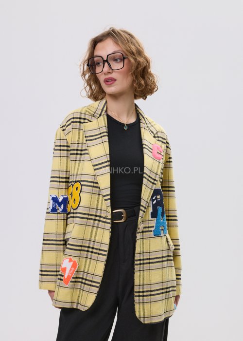 Marynarka damska w żółtą kratę z kolorowymi naszywkami literowymi, o luźnym kroju z klapami, stylizowany z czarnym topem i spodniami.