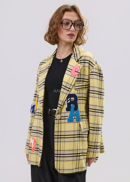Marynarka damska w żółtą kratę z kolorowymi naszywkami literowymi, o luźnym kroju z klapami, stylizowany z czarnym topem i spodniami.