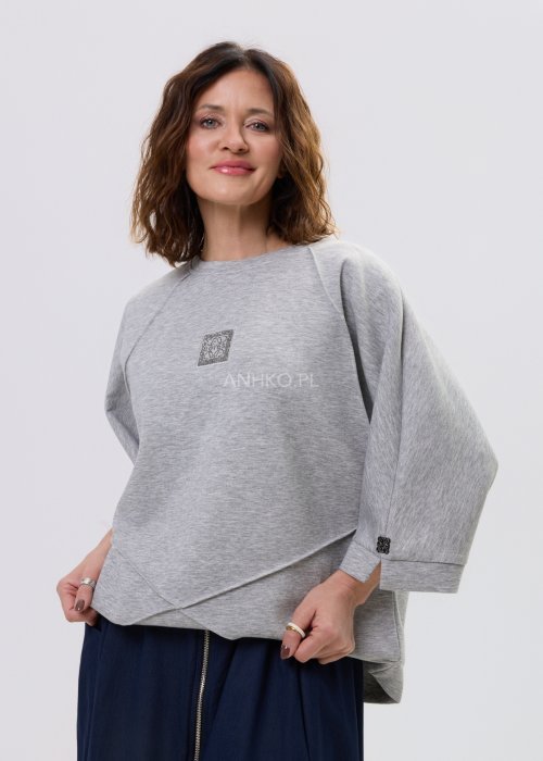 Szara bluza damska oversize z krótkim rękawem typu kimono i asymetrycznym dołem, wykonana z miękkiej dzianiny, stylizowana ze spódnicą.