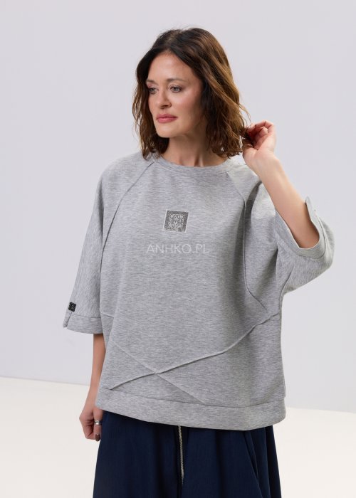 Szara bluza damska oversize z krótkim rękawem typu kimono i asymetrycznym dołem, wykonana z miękkiej dzianiny, stylizowana ze spódnicą.