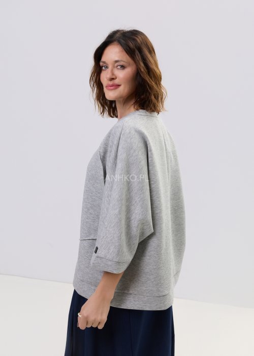 Szara bluza damska oversize z krótkim rękawem typu kimono i asymetrycznym dołem, wykonana z miękkiej dzianiny, stylizowana ze spódnicą.