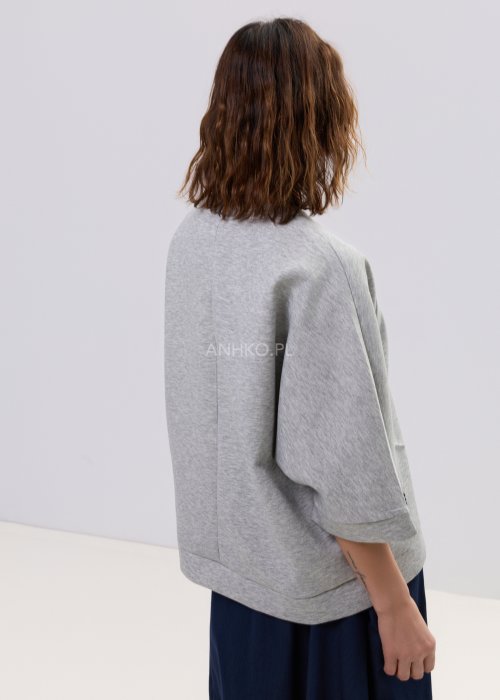 Szara bluza damska oversize z krótkim rękawem typu kimono i asymetrycznym dołem, wykonana z miękkiej dzianiny, stylizowana ze spódnicą.