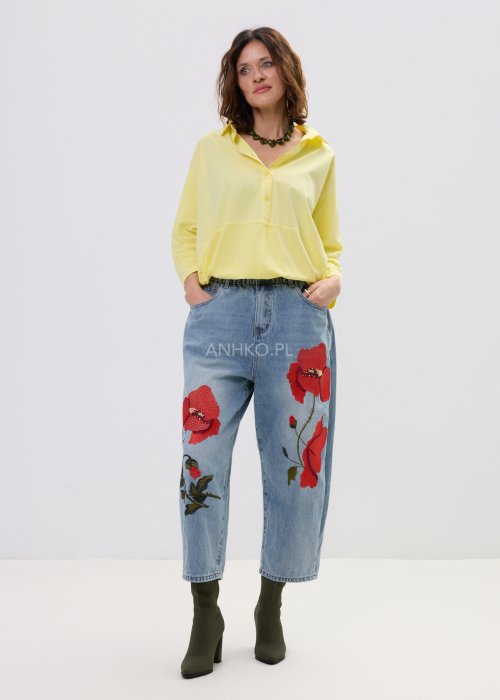 Żółta koszula damska oversize z kołnierzykiem i dekoltem polo, o luźnym kroju z długim rękawem, zestawiona z jeansami w stylu casual.