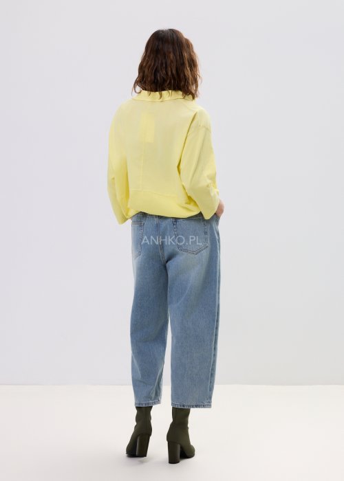 Żółta koszula damska oversize z kołnierzykiem i dekoltem polo, o luźnym kroju z długim rękawem, zestawiona z jeansami w stylu casual.