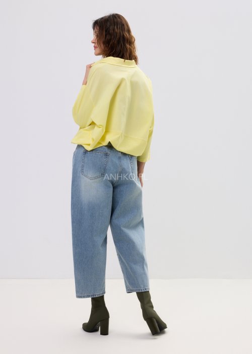 Żółta koszula damska oversize z kołnierzykiem i dekoltem polo, o luźnym kroju z długim rękawem, zestawiona z jeansami w stylu casual.