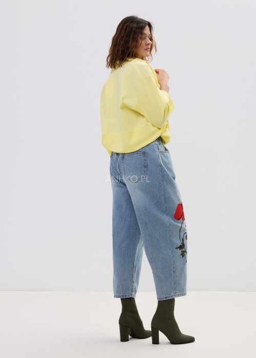 Żółta koszula damska oversize z kołnierzykiem i dekoltem polo, o luźnym kroju z długim rękawem, zestawiona z jeansami w stylu casual.