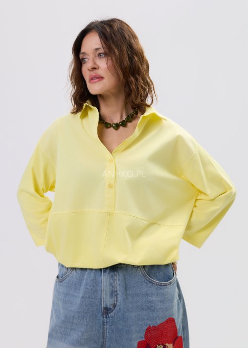 Żółta koszula damska oversize z kołnierzykiem i dekoltem polo, o luźnym kroju z długim rękawem, zestawiona z jeansami w stylu casual.