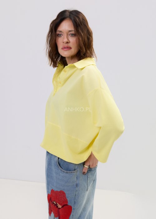 Żółta koszula damska oversize z kołnierzykiem i dekoltem polo, o luźnym kroju z długim rękawem, zestawiona z jeansami w stylu casual.