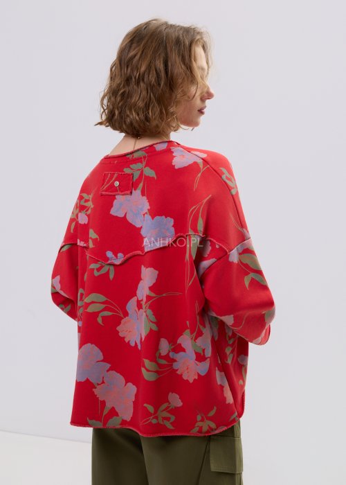 Czerwona bluza damska w kwiaty o luźnym kroju z długim rękawem i kieszonką na piersi, zestawiona z oliwkowymi spodniami w stylu casual.