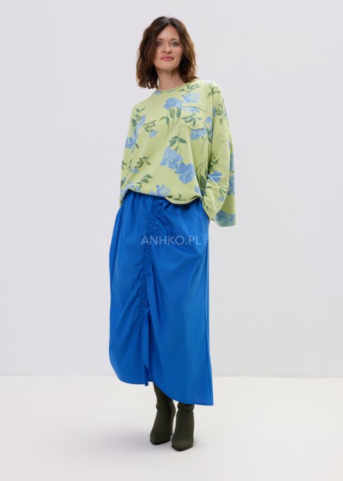 Zielona bluza damska w niebieskie kwiaty o luźnym kroju z długim rękawem i kieszonką na piersi, zestawiona z niebieską spódnicą w stylu casual.