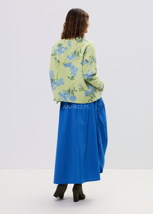 Zielona bluza damska w niebieskie kwiaty o luźnym kroju z długim rękawem i kieszonką na piersi, zestawiona z niebieską spódnicą w stylu casual.