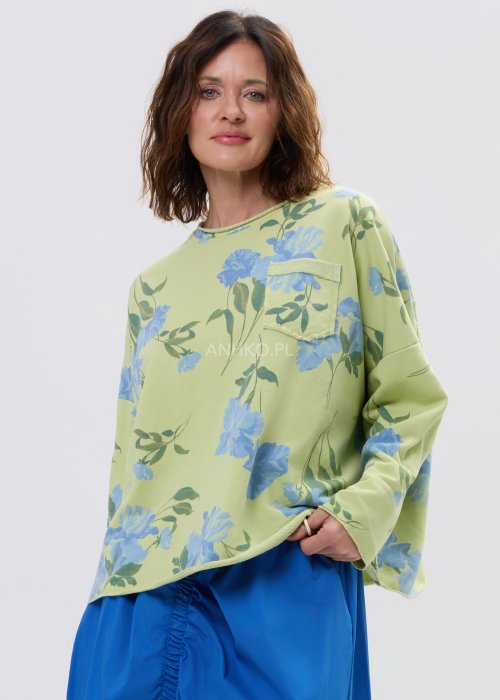 Zielona bluza damska w niebieskie kwiaty o luźnym kroju z długim rękawem i kieszonką na piersi, zestawiona z niebieską spódnicą w stylu casual.