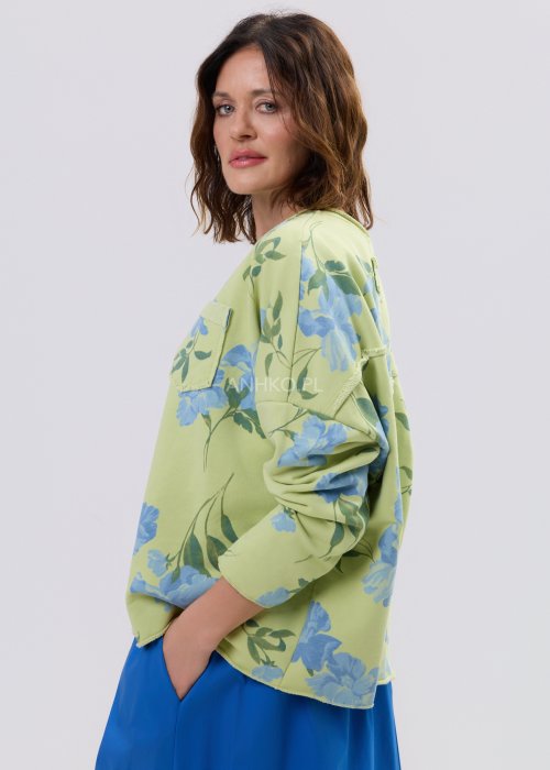 Zielona bluza damska w niebieskie kwiaty o luźnym kroju z długim rękawem i kieszonką na piersi, zestawiona z niebieską spódnicą w stylu casual.