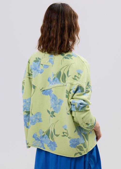 Zielona bluza damska w niebieskie kwiaty o luźnym kroju z długim rękawem i kieszonką na piersi, zestawiona z niebieską spódnicą w stylu casual.