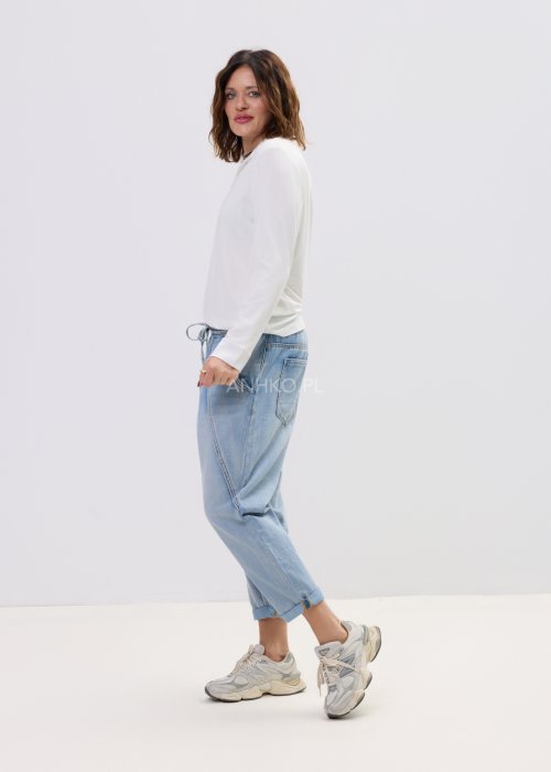 Biała bluzka damska z długim rękawem i dekoltem w stylu polo, o gładkim wykończeniu, zestawiona z jasnymi jeansami w casualowej stylizacji.