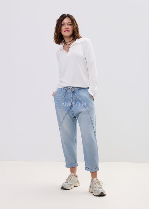 Biała bluzka damska z długim rękawem i dekoltem w stylu polo, o gładkim wykończeniu, zestawiona z jasnymi jeansami w casualowej stylizacji.