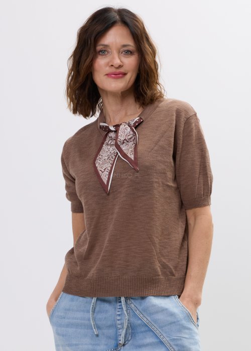 Brązowa bluzka dzianinowa damska z krótkim rękawem i wiązaną apaszką przy dekolcie, o klasycznym kroju, zestawiona z jasnymi jeansami w stylu casual.