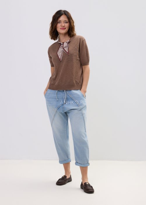 Brązowa bluzka dzianinowa damska z krótkim rękawem i wiązaną apaszką przy dekolcie, o klasycznym kroju, zestawiona z jasnymi jeansami w stylu casual.