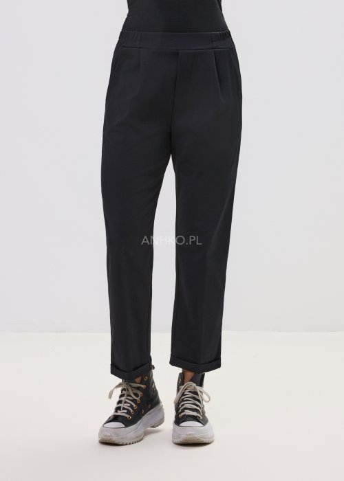 Czarne spodnie damskie z prostą nogawką i elastycznym pasem, o minimalistycznym fasonie, zestawione ze sneakersami w codziennej stylizacji.