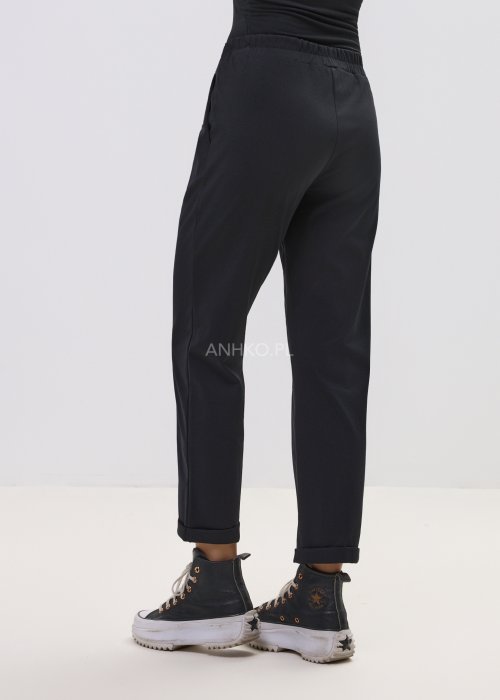 Czarne spodnie damskie z prostą nogawką i elastycznym pasem, o minimalistycznym fasonie, zestawione ze sneakersami w codziennej stylizacji.