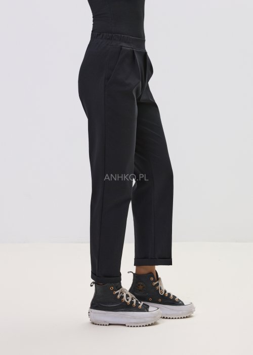 Czarne spodnie damskie z prostą nogawką i elastycznym pasem, o minimalistycznym fasonie, zestawione ze sneakersami w codziennej stylizacji.