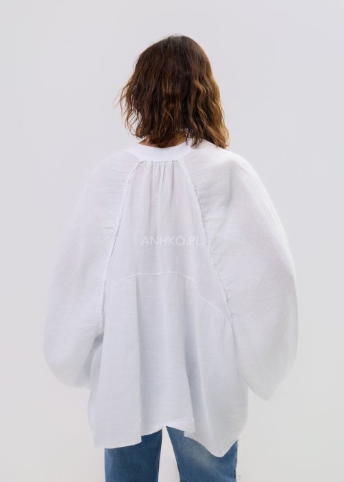 Biała lniana koszula damska oversize z długim rękawem i lekkim, zwiewnym materiałem, stylizowana z jeansami i biżuterią w casualowym looku.