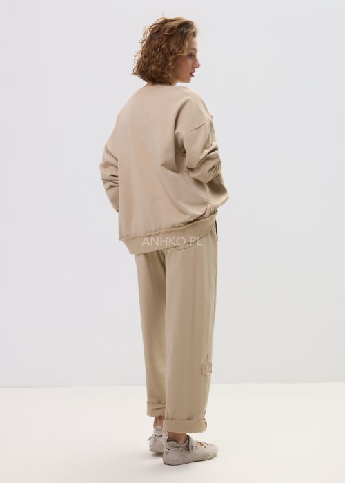 Beżowe spodnie damskie o luźnym kroju z elastycznym pasem i ozdobnymi naszyciami na nogawce.