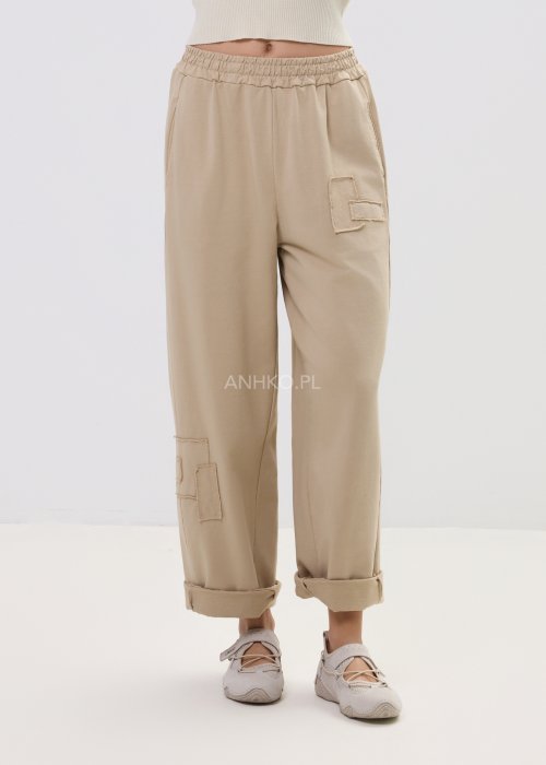 Beżowe spodnie damskie o luźnym kroju z elastycznym pasem i ozdobnymi naszyciami na nogawce.