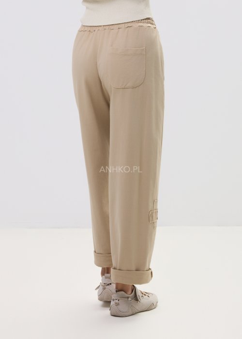 Beżowe spodnie damskie o luźnym kroju z elastycznym pasem i ozdobnymi naszyciami na nogawce.