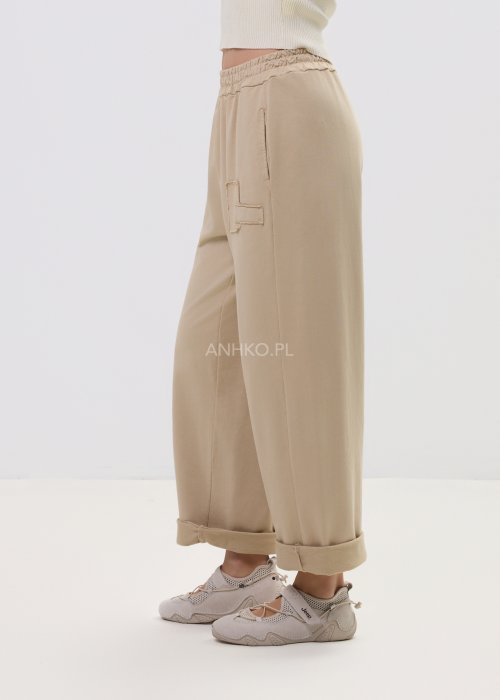 Beżowe spodnie damskie o luźnym kroju z elastycznym pasem i ozdobnymi naszyciami na nogawce.