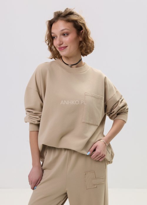 Beżowa bluza damska o luźnym kroju z kieszonką na piersi i długimi rękawami zakończonymi ściągaczem.