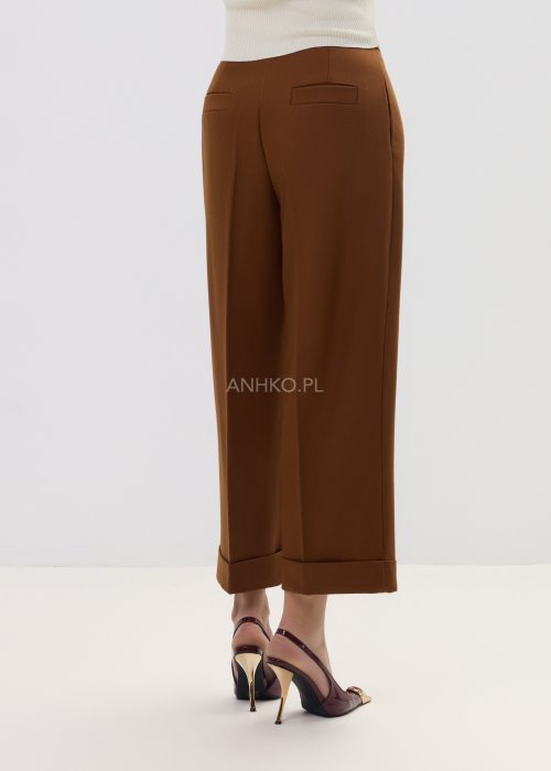 Karmelowe eleganckie spodnie damskie o szerokim kroju z wysokim stanem i podwiniętą nogawką.