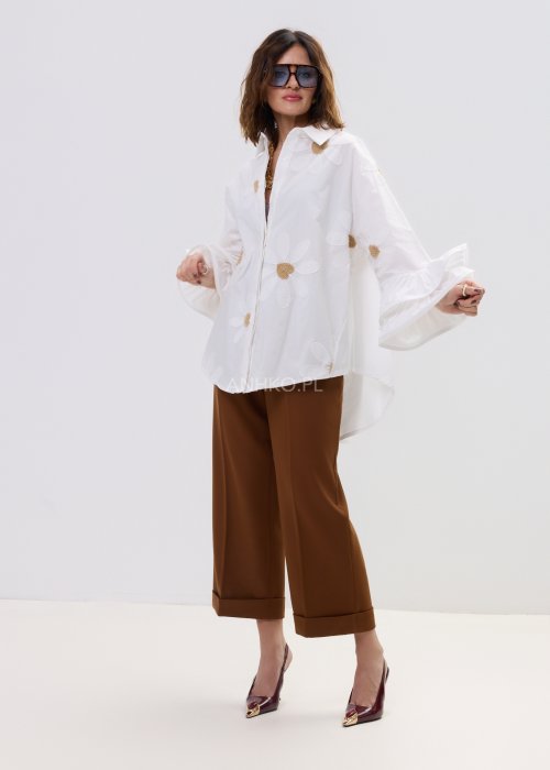 Biała koszula damska oversize z haftowanymi stokrotkami i szerokimi, falującymi rękawami.