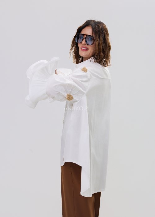 Biała koszula damska oversize z haftowanymi stokrotkami i szerokimi, falującymi rękawami.