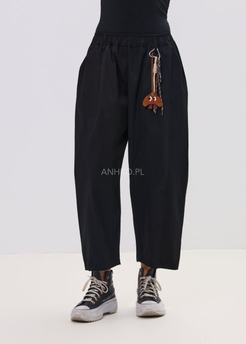 Czarne spodnie damskie o luźnym, nowoczesnym kroju z elastycznym pasem i szeroką nogawką. Model ozdobiony dekoracyjnym brelokiem przy pasie, idealny do codziennych, casualowych stylizacji.