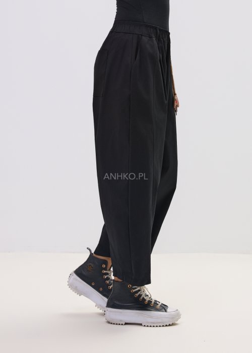 Czarne spodnie damskie o luźnym, nowoczesnym kroju z elastycznym pasem i szeroką nogawką. Model ozdobiony dekoracyjnym brelokiem przy pasie, idealny do codziennych, casualowych stylizacji.