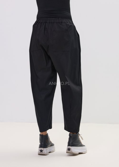 Czarne spodnie damskie o luźnym, nowoczesnym kroju z elastycznym pasem i szeroką nogawką. Model ozdobiony dekoracyjnym brelokiem przy pasie, idealny do codziennych, casualowych stylizacji.