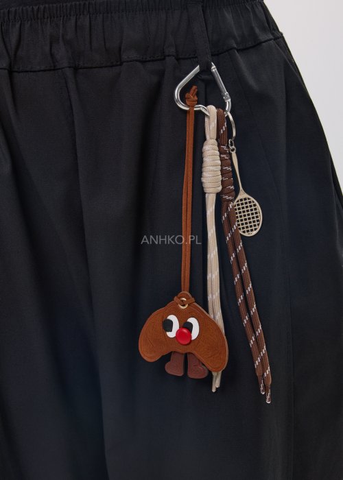 Czarne spodnie damskie o luźnym, nowoczesnym kroju z elastycznym pasem i szeroką nogawką. Model ozdobiony dekoracyjnym brelokiem przy pasie, idealny do codziennych, casualowych stylizacji.