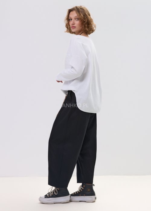 Czarne spodnie damskie o luźnym, nowoczesnym kroju z elastycznym pasem i szeroką nogawką. Model ozdobiony dekoracyjnym brelokiem przy pasie, idealny do codziennych, casualowych stylizacji.