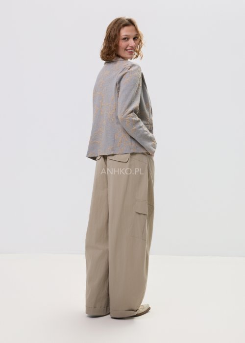 Beżowo-szary żakiet damski w delikatny roślinny wzór, zapinany na guziki, z klasycznymi klapami i prostym fasonem. Elegancka marynarka w stylu smart casual zestawiona z jasnymi spodniami cargo.