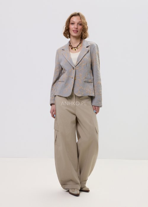 Beżowo-szary żakiet damski w delikatny roślinny wzór, zapinany na guziki, z klasycznymi klapami i prostym fasonem. Elegancka marynarka w stylu smart casual zestawiona z jasnymi spodniami cargo.