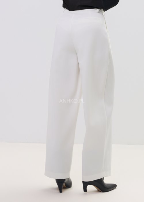 Białe spodnie damskie garniturowe z wysokim stanem, zapinane na guzik, z eleganckimi zakładkami z przodu. Szeroka, lekko zwężana nogawka nadaje im nowoczesny, elegancki charakter.