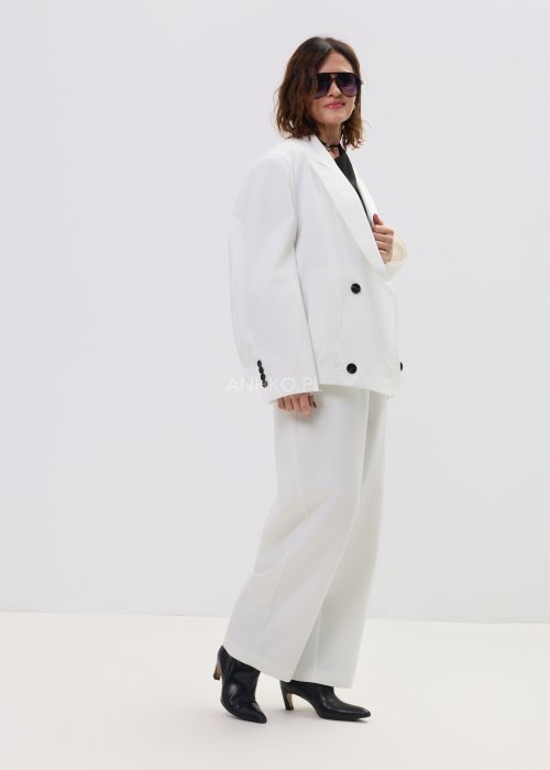 Białe spodnie damskie garniturowe z wysokim stanem, zapinane na guzik, z eleganckimi zakładkami z przodu. Szeroka, lekko zwężana nogawka nadaje im nowoczesny, elegancki charakter.